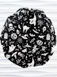 A black and white Halloween-themed Bouffant style surgical scrub cap by JensCaps with a printed pattern of ghosts, witches, pumpkins, and stars and displayed on a white mannequin head 