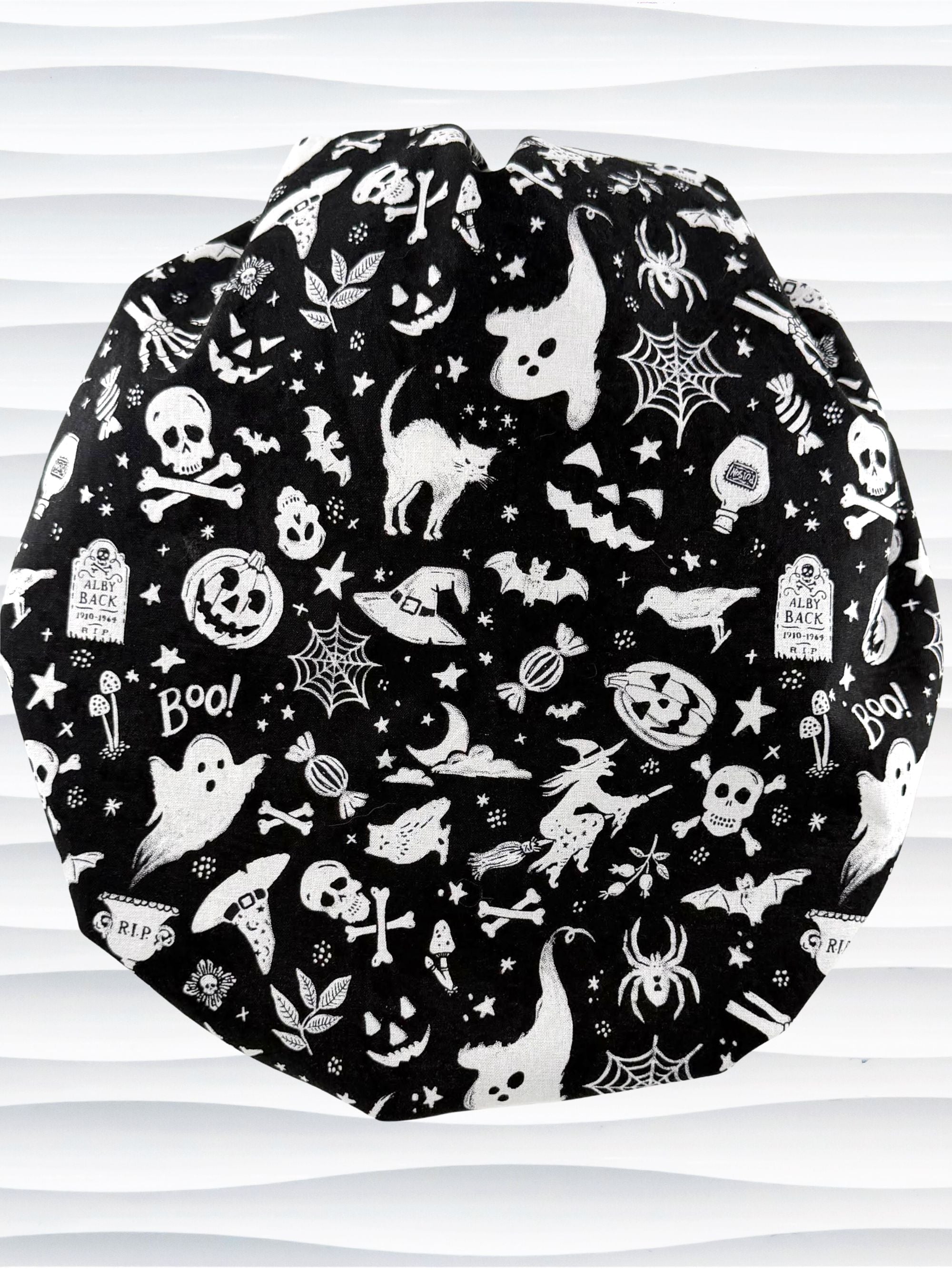 A black and white Halloween-themed Bouffant style surgical scrub cap by JensCaps with a printed pattern of ghosts, witches, pumpkins, and stars and displayed on a white mannequin head 