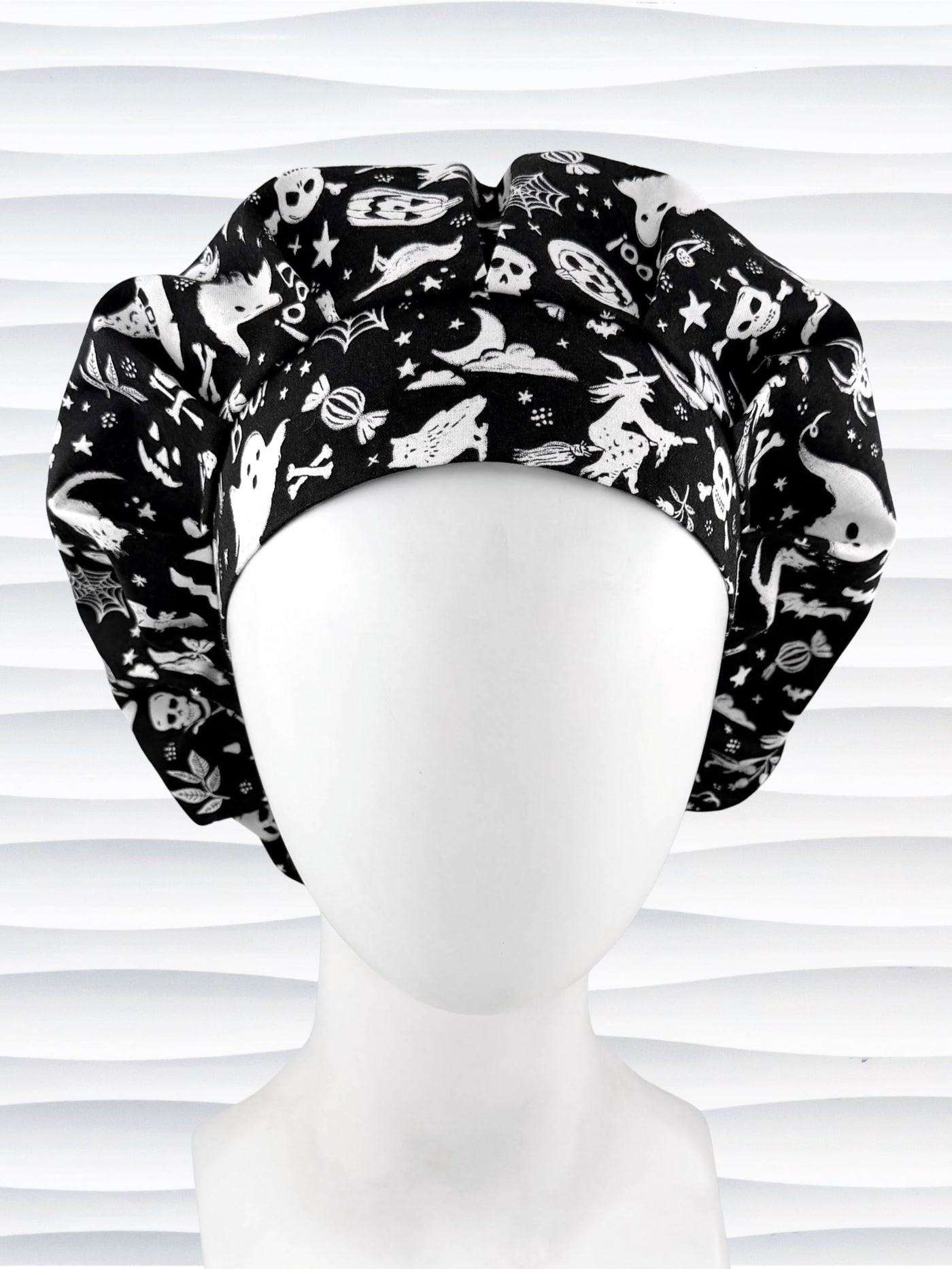 A black and white Halloween-themed Bouffant style surgical scrub cap by JensCaps with a printed pattern of ghosts, witches, pumpkins, and stars and displayed on a white mannequin head 