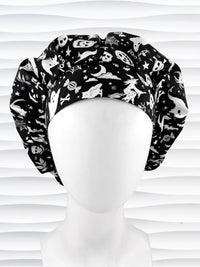A black and white Halloween-themed Bouffant style surgical scrub cap by JensCaps with a printed pattern of ghosts, witches, pumpkins, and stars and displayed on a white mannequin head 