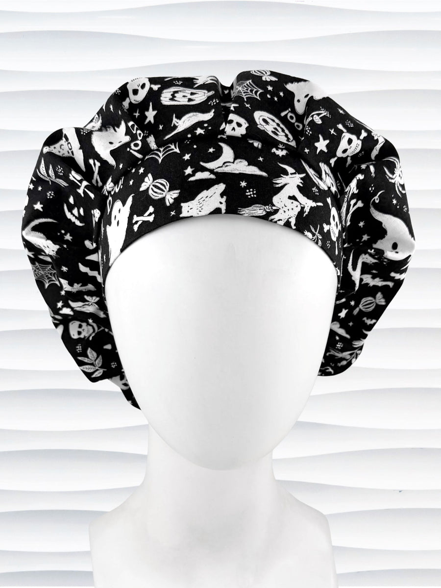 A black and white Halloween-themed Bouffant style surgical scrub cap by JensCaps with a printed pattern of ghosts, witches, pumpkins, and stars and displayed on a white mannequin head 
