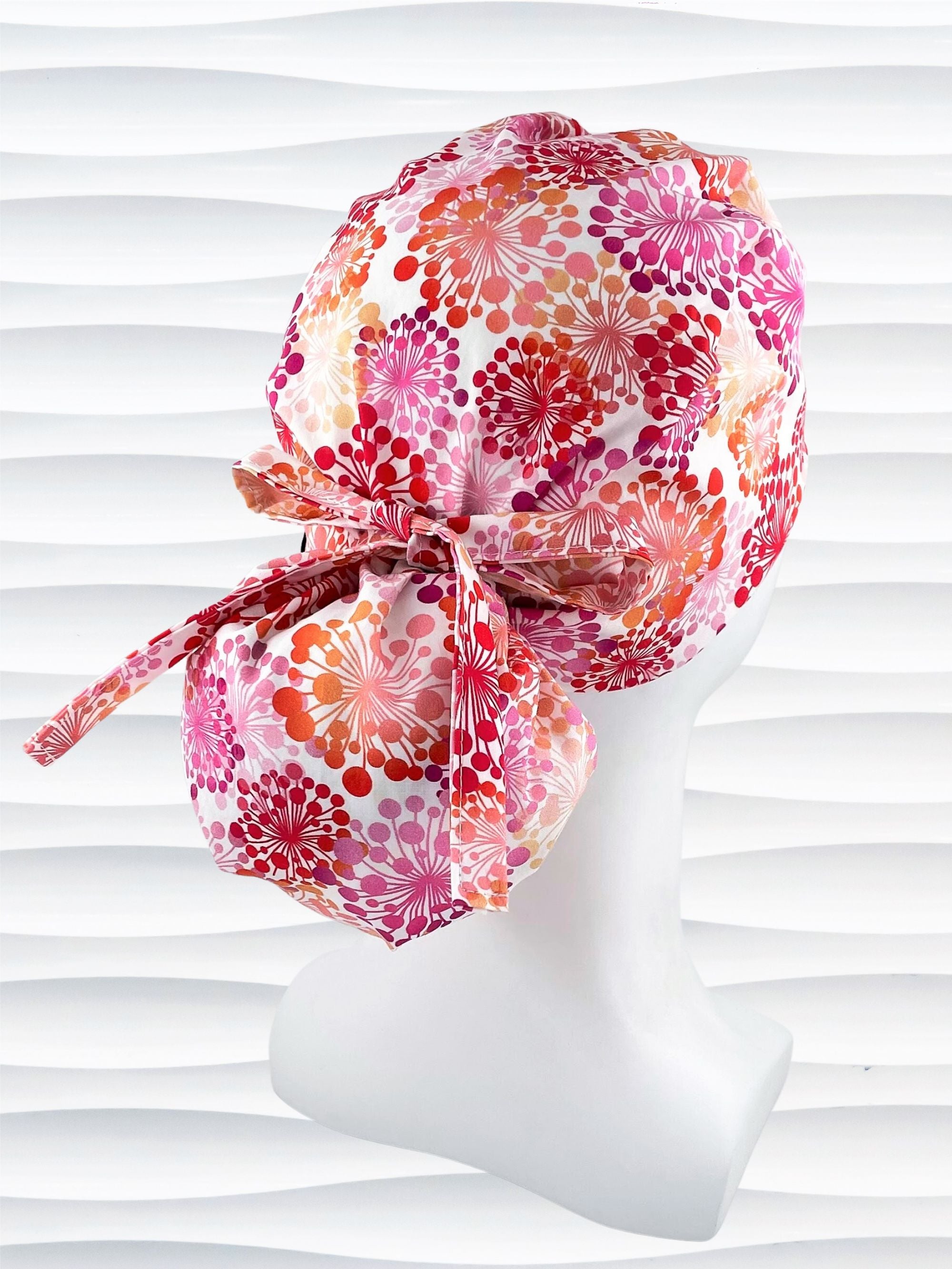 Ponytail style scrub cap with pink and red and orange allium flowers on white cotton fabric and finished with choice of grosgrain ribbon color