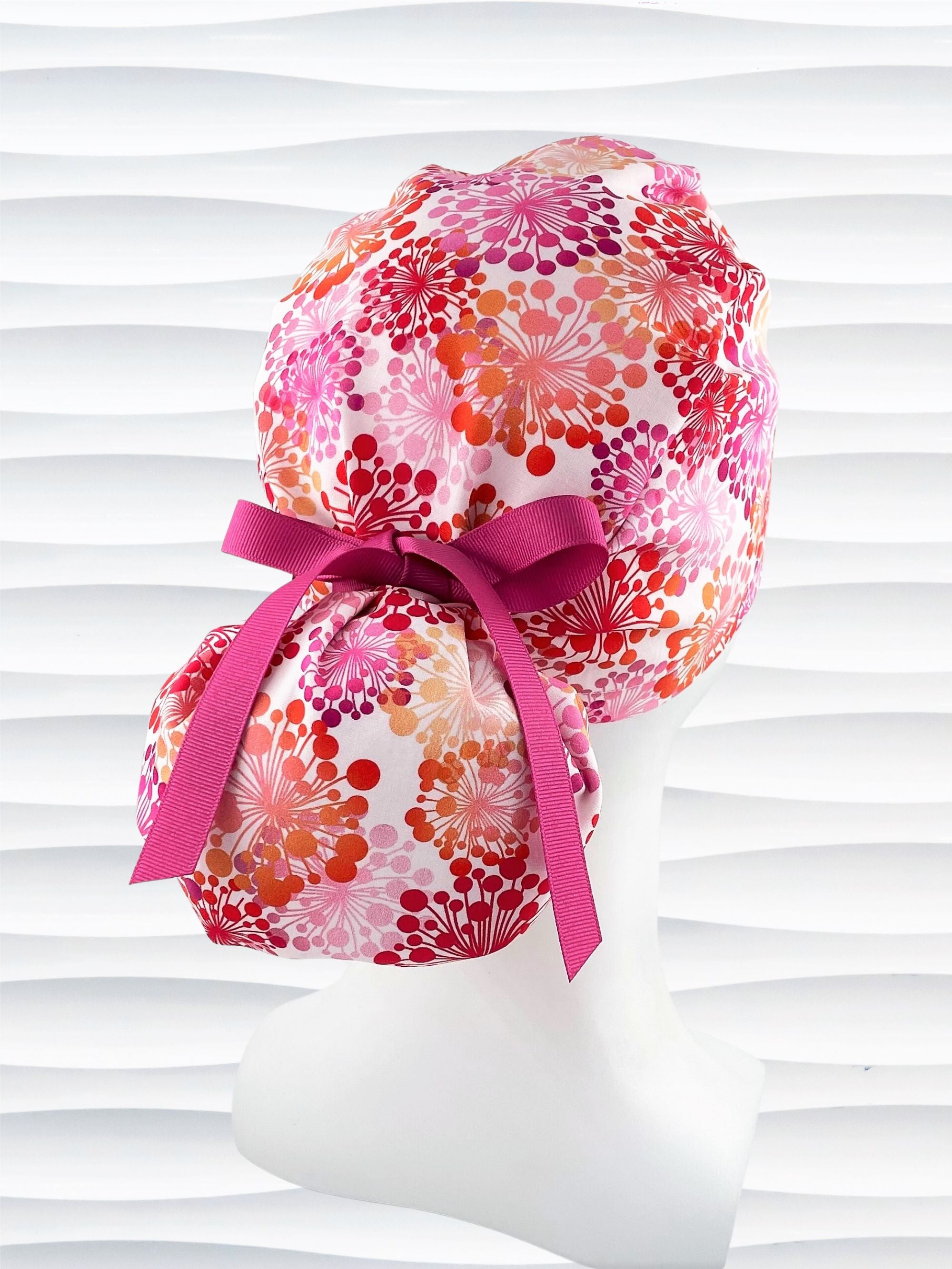 Ponytail style scrub cap with pink and red and orange allium flowers on white cotton fabric and finished with choice of grosgrain ribbon color