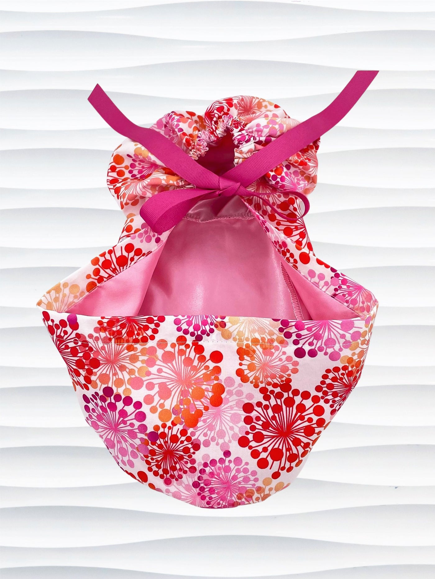 Ponytail style scrub cap with pink and red and orange allium flowers on white cotton fabric and finished with choice of grosgrain ribbon color and satin lining option