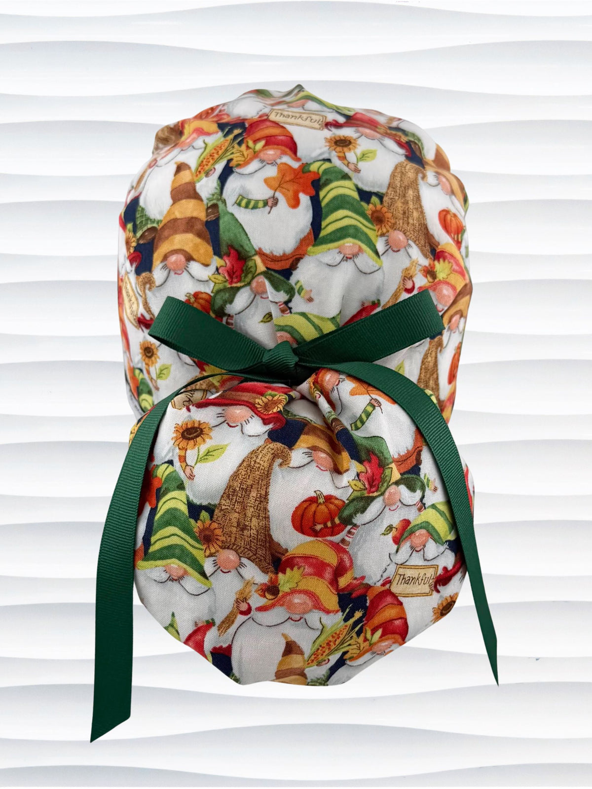Ponytail style surgical scrub cap with gnomes in fall colors holding sunflowers and signs that say thankful, tied with a ribbon, and displayed on a mannequin head.