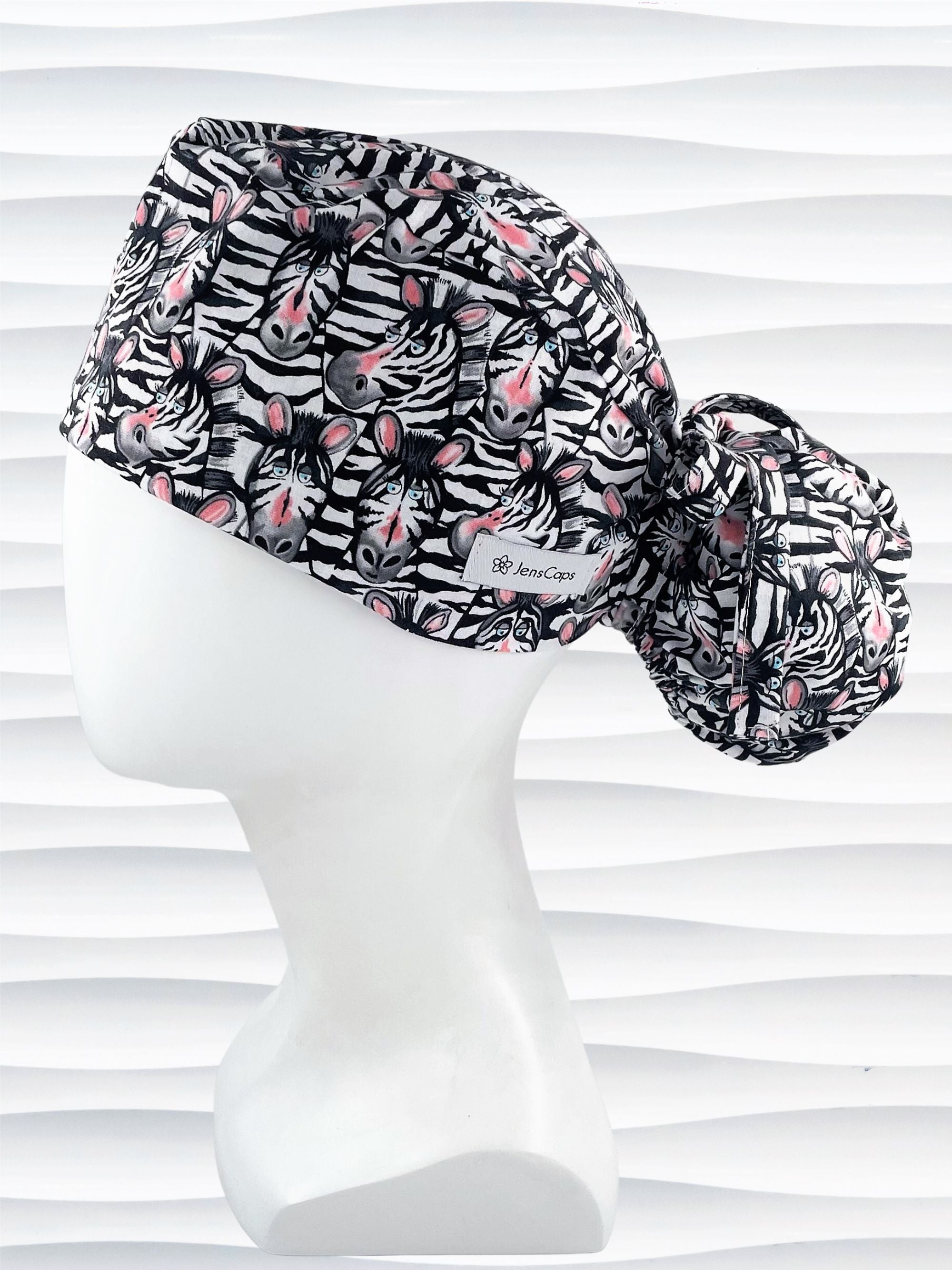 Ponytail style surgical scrub cap with black and white zebras with pink faces on premium cotton fabric.