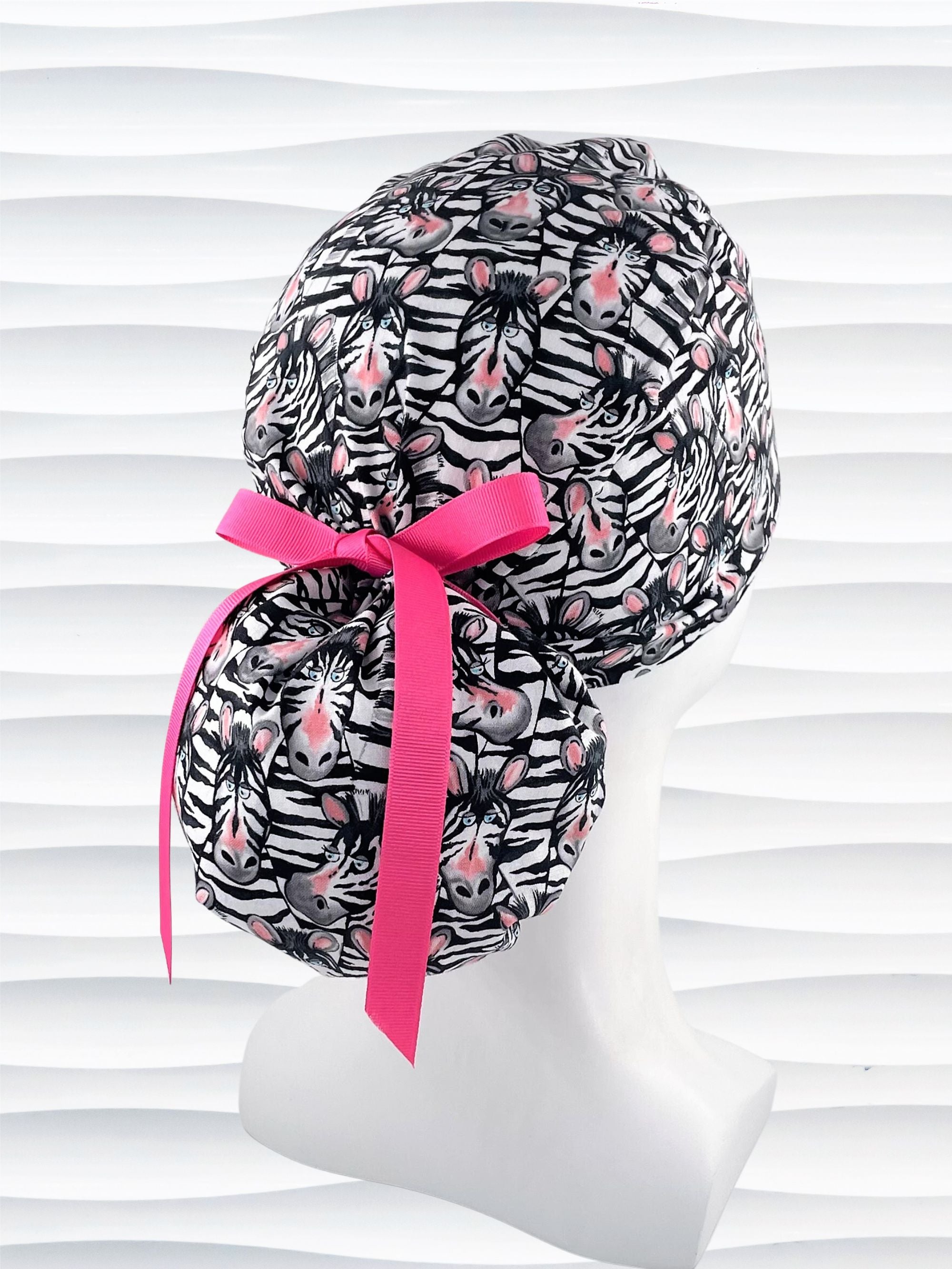 Ponytail style surgical scrub cap with black and white zebras with pink faces on premium cotton fabric.