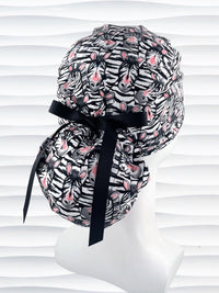 Ponytail style surgical scrub cap with black and white zebras with pink faces on premium cotton fabric.