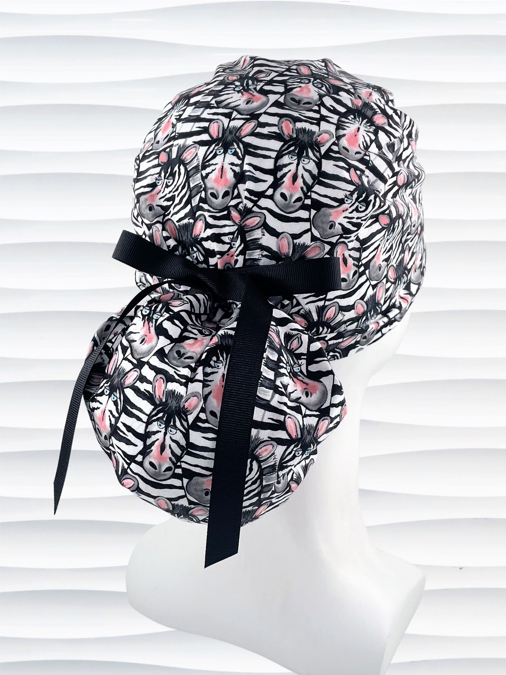 Ponytail style surgical scrub cap with black and white zebras with pink faces on premium cotton fabric.