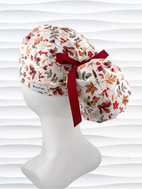 Ponytail style surgical scrub cap with an assortment of autumn eaves in fall colors all over a light background, finished with a ribbon tie, and displayed on a white mannequin head.
