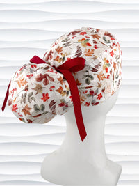 Ponytail style surgical scrub cap with an assortment of autumn eaves in fall colors all over a light background, finished with a ribbon tie, and displayed on a white mannequin head.