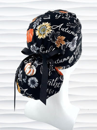 Ponytail style surgical scrub cap hat with pumpkins, sunflowers, leaves, and autumn themed words all over black cotton fabric.