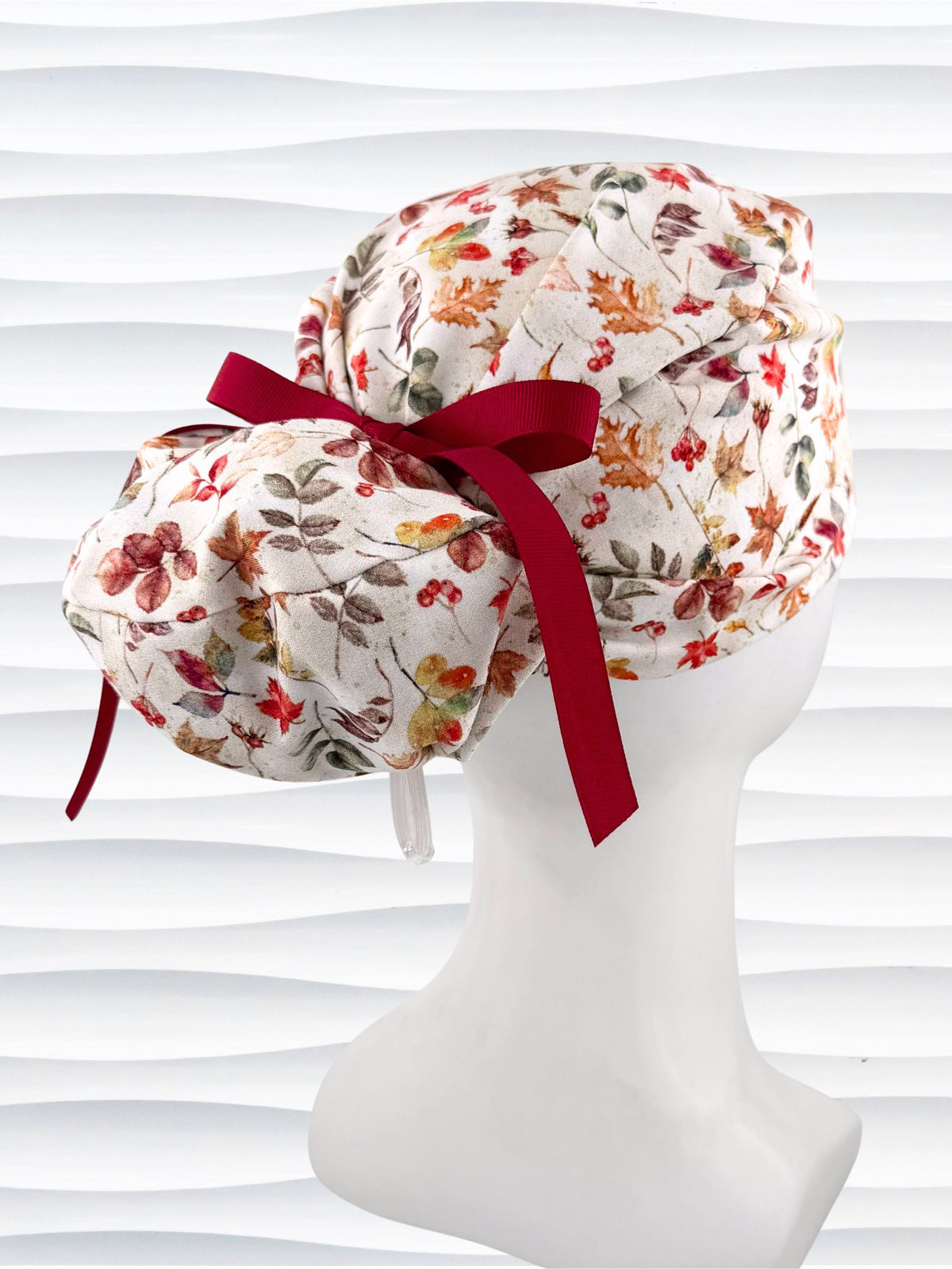 Euro Pony style surgical scrub cap with an assortment of autumn eaves in fall colors all over a light background, finished with a ribbon tie, and displayed on a white mannequin head.