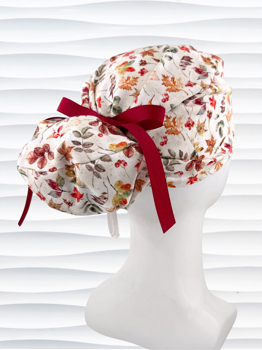 Euro Pony style surgical scrub cap with an assortment of autumn eaves in fall colors all over a light background, finished with a ribbon tie, and displayed on a white mannequin head.