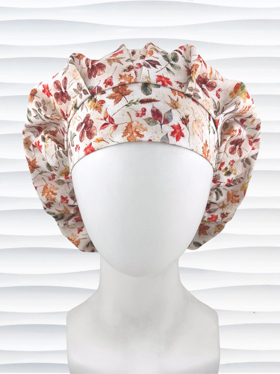 Bouffant style surgical scrub cap with an assortment of autumn eaves in fall colors all over a light background and displayed on a white mannequin head.