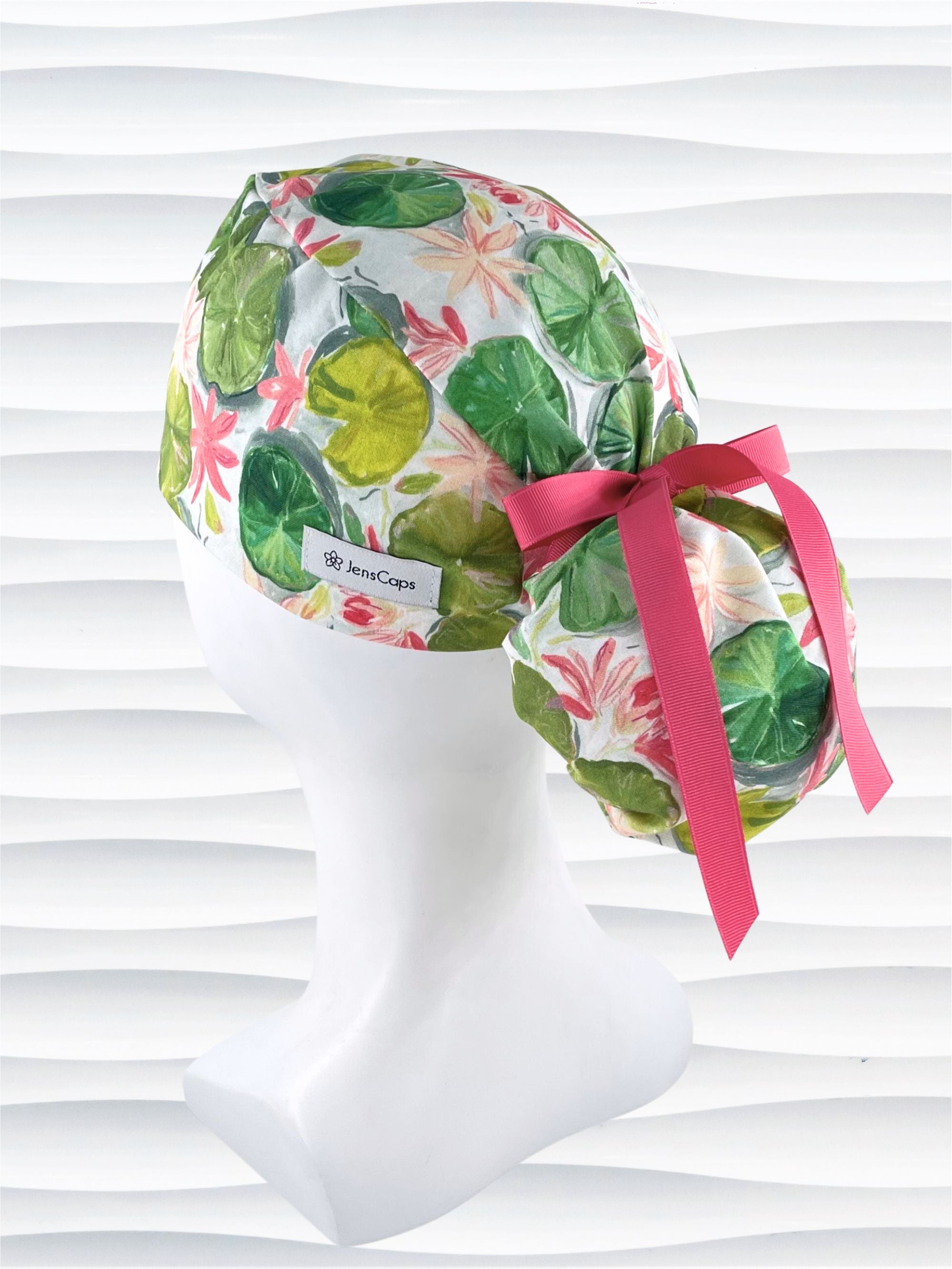 Ponytail style surgical Scrub Cap hat for long or medium hair with lilies floating on a lily pond in pinks and greens on a white cotton fabric.