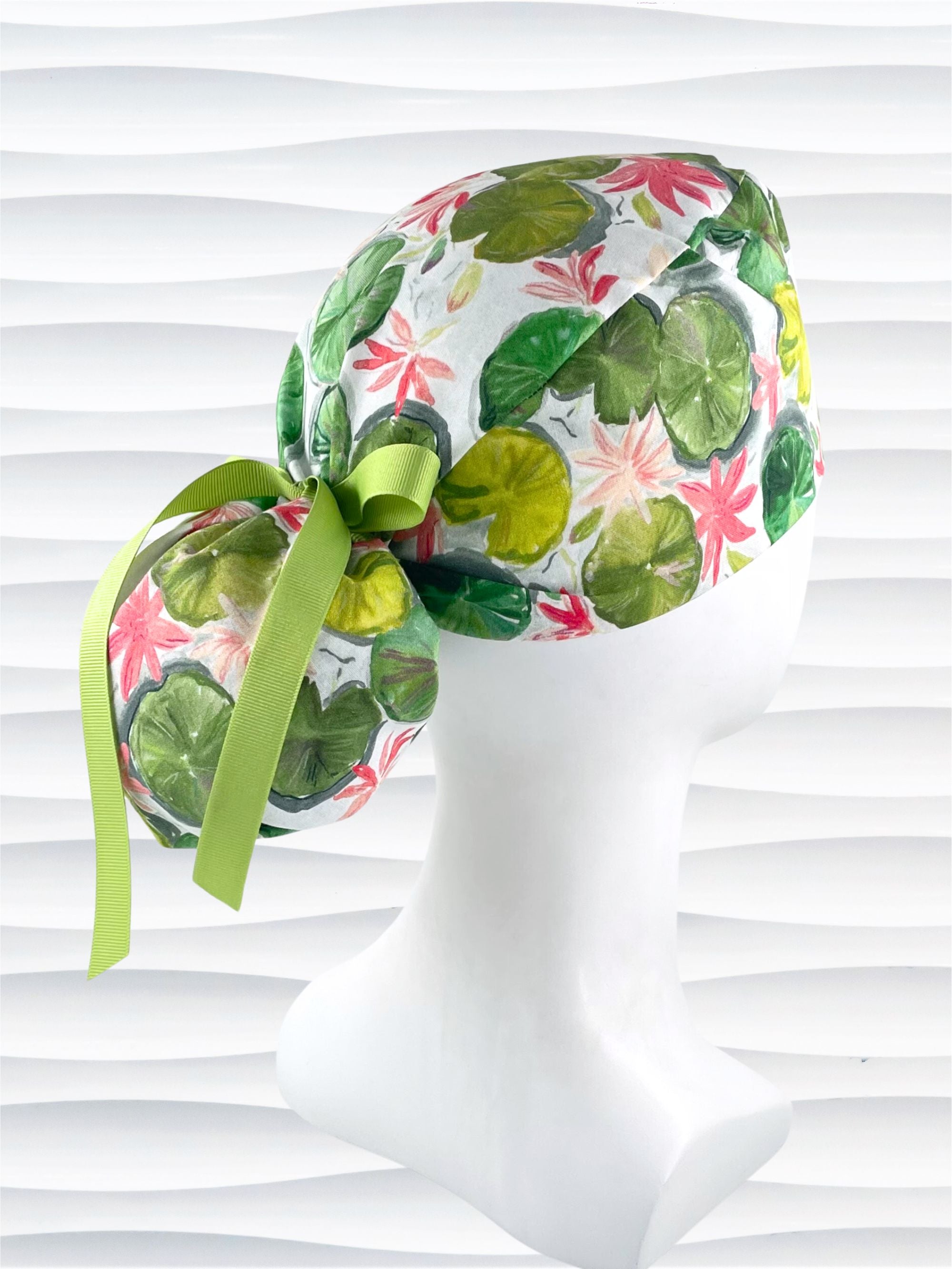 Ponytail style surgical Scrub Cap hat for long or medium hair with lilies floating on a lily pond in pinks and greens on a white cotton fabric.