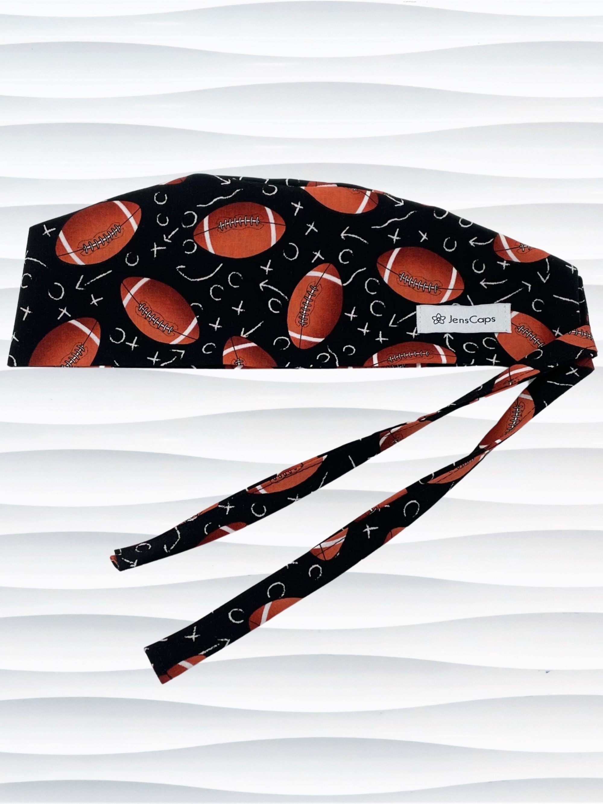 Surgeon style surgical scrub cap hat with footballs and Xs and Os tossed all over this black cotton premium fabric.
