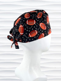 Surgeon style surgical scrub cap hat with footballs and Xs and Os tossed all over this black cotton premium fabric.