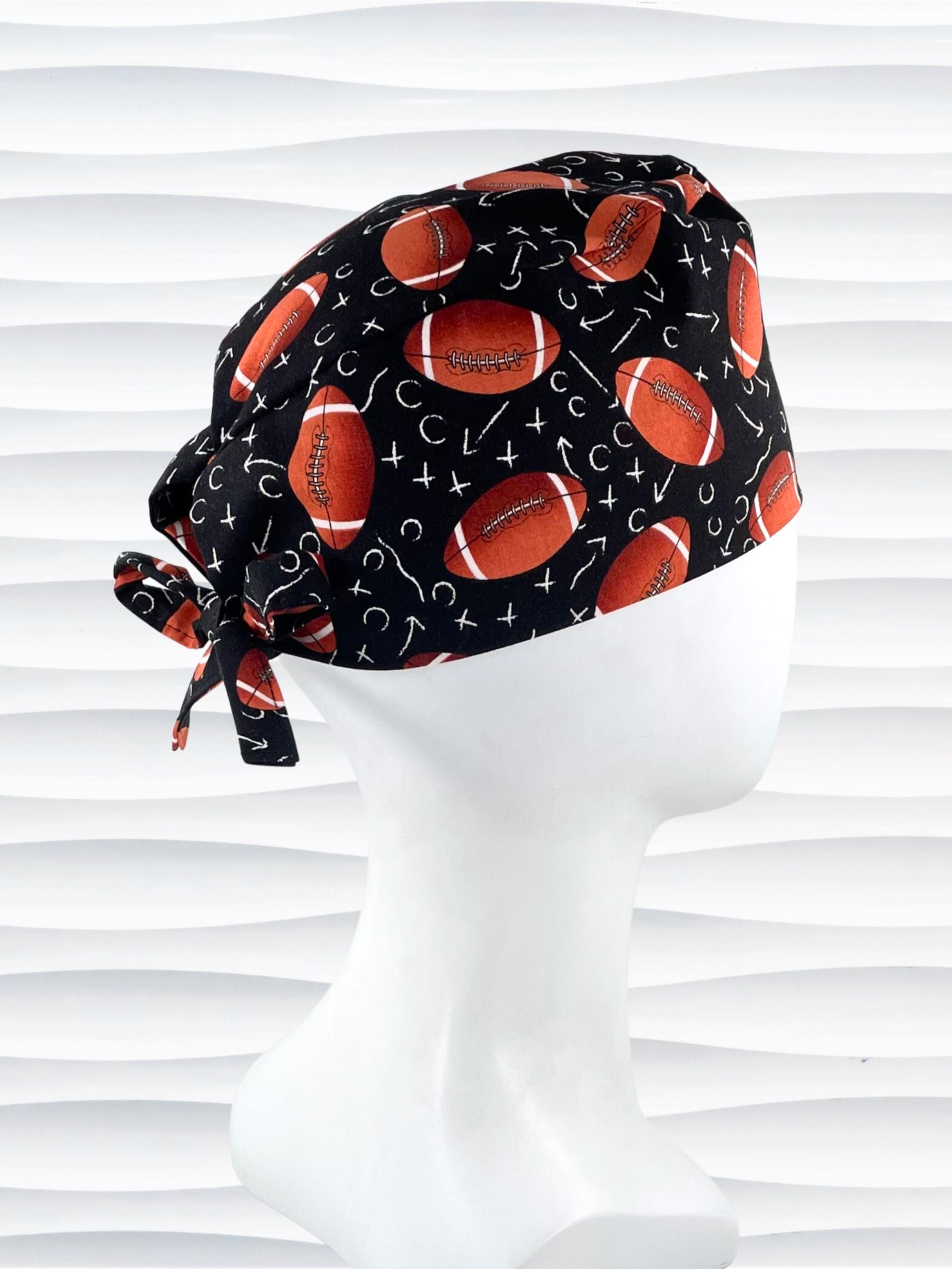 Surgeon style surgical scrub cap hat with footballs and Xs and Os tossed all over this black cotton premium fabric.