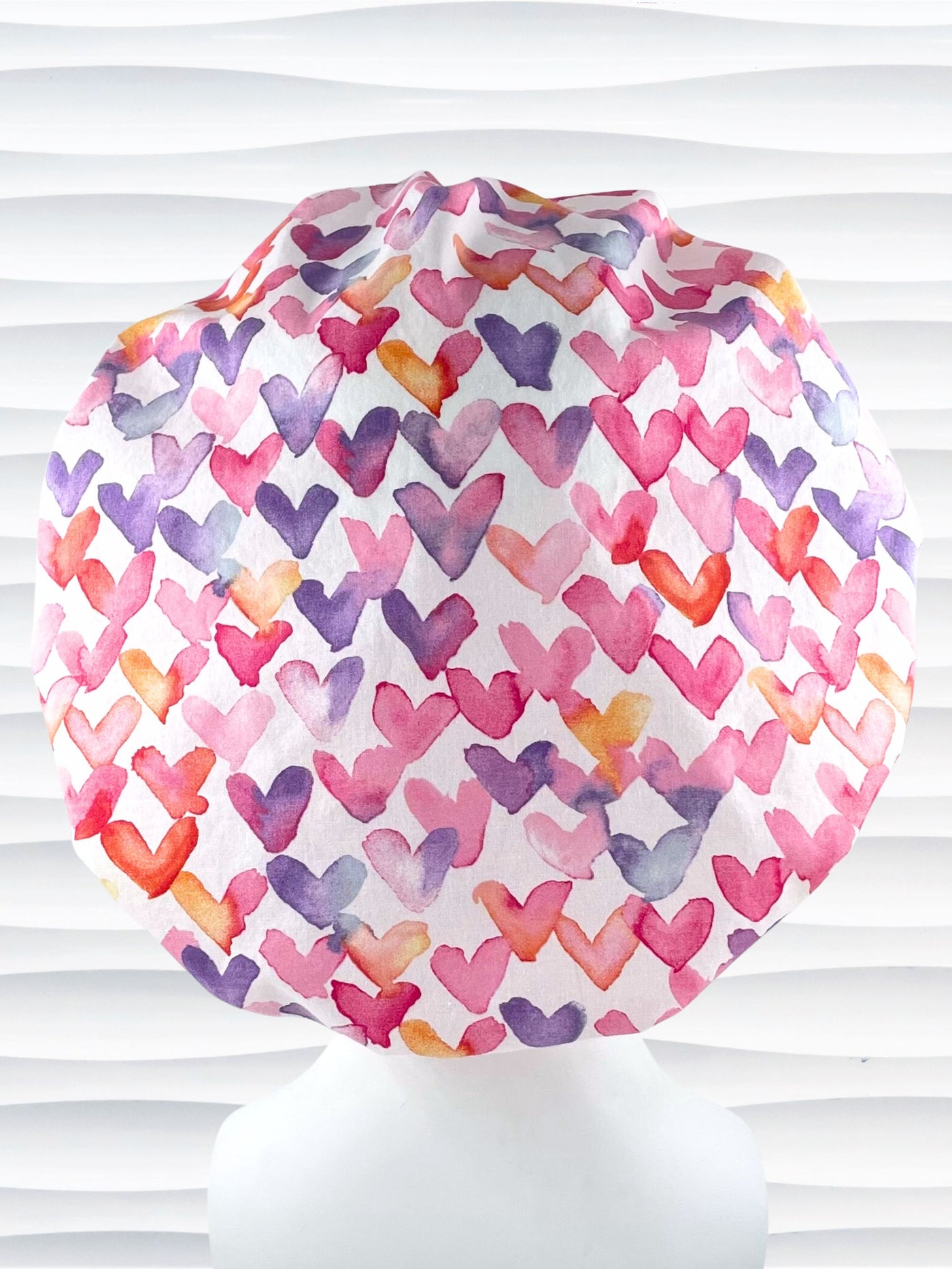 Bouffant style surgical scrub cap by JensCaps with watercolor hearts in pastel colors all over white cotton fabric and dispoayed on a white mannequin head.