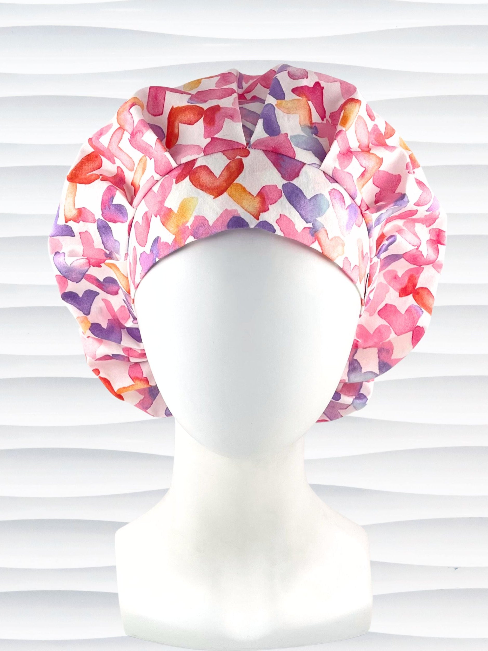 Bouffant style surgical scrub cap by JensCaps with watercolor hearts in pastel colors all over white cotton fabric and dispoayed on a white mannequin head.