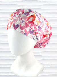 Bouffant style surgical scrub cap by JensCaps with watercolor hearts in pastel colors all over white cotton fabric and dispoayed on a white mannequin head.