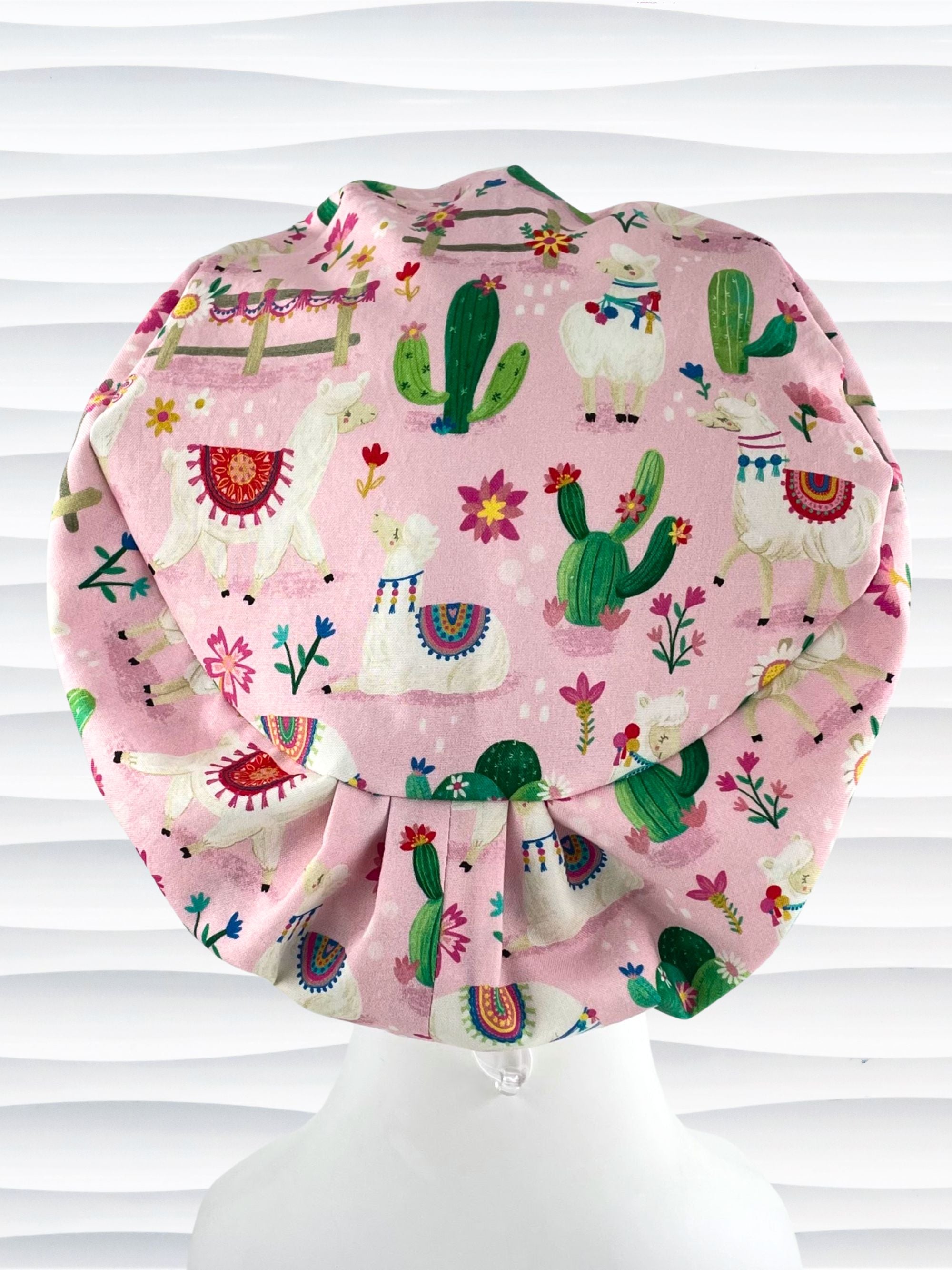 Pixie Euro style surgical scrub cap hat with white llamas wearing blankets, pink and blue flowers, and green cactus on pink cotton fabric.