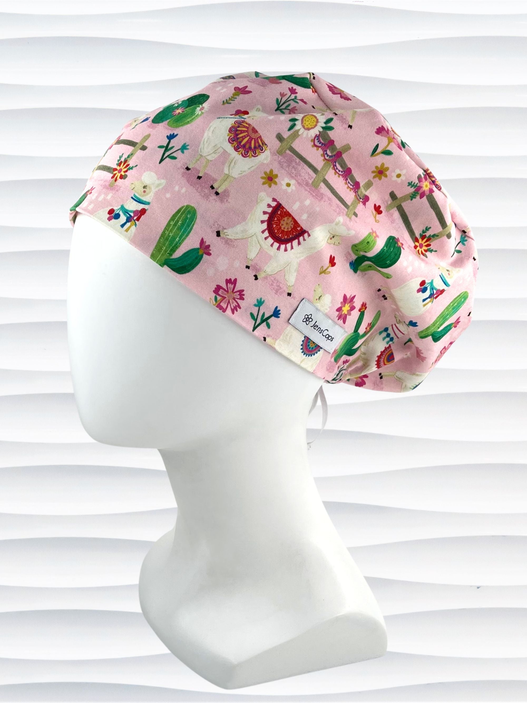 Pixie Euro style surgical scrub cap hat with white llamas wearing blankets, pink and blue flowers, and green cactus on pink cotton fabric.