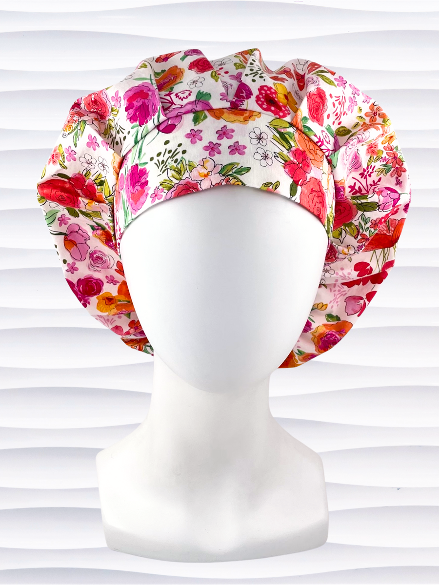 Bouffant style surgical scrub cap hat with pink, red, yellow, white, and orange flowers on white cotton fabric.