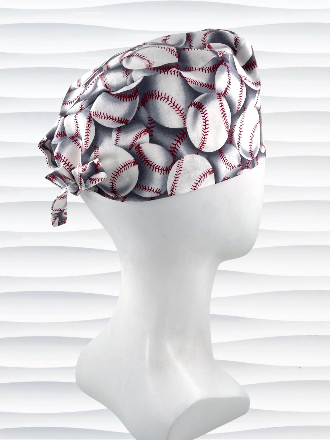 Surgeon style surgical scrub cap hat with an allover print of white baseballs with red stitching and gray shadows on cotton fabric.