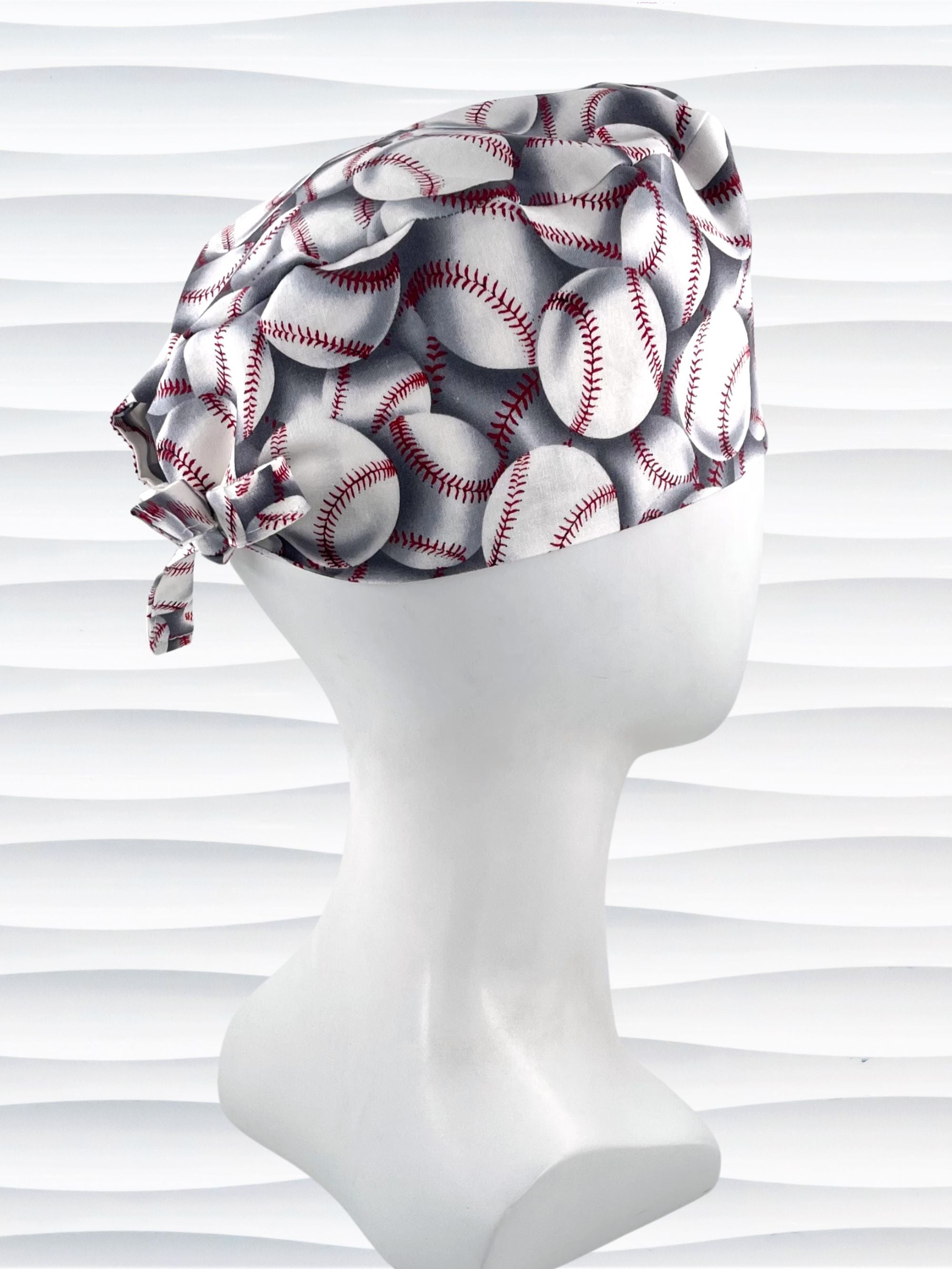 Surgeon style surgical scrub cap hat with an allover print of white baseballs with red stitching and gray shadows on cotton fabric.