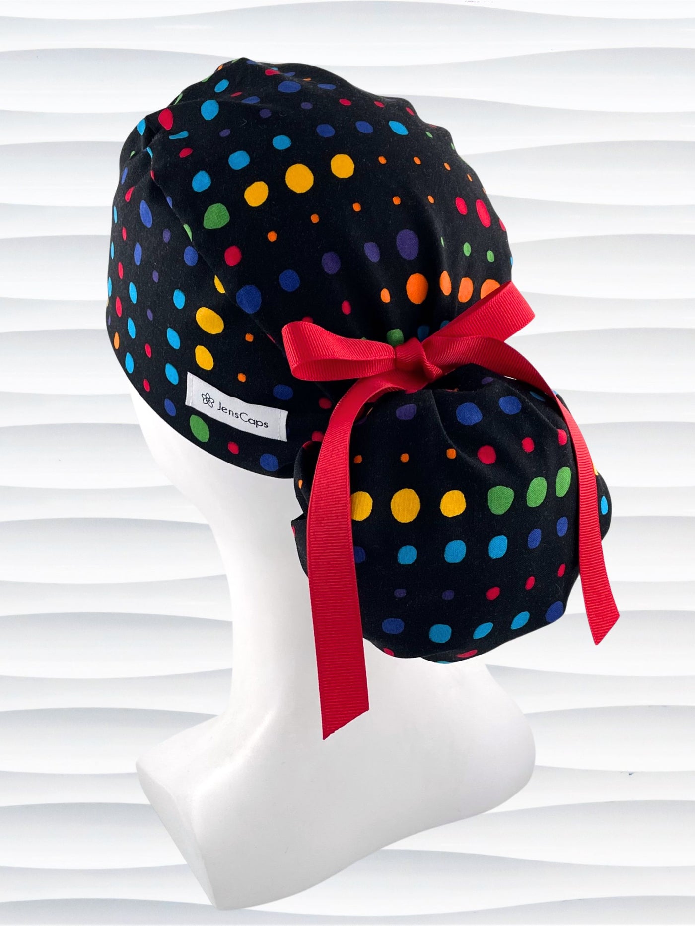 Ponytail style surgical scrub cap hat with circles in primary colors in a linear design on black cotton fabric.