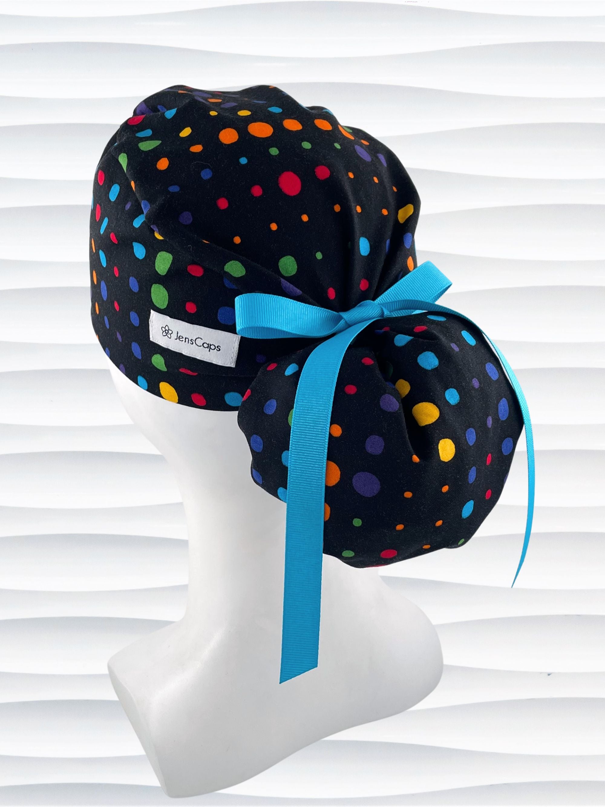 Ponytail style surgical scrub cap hat with circles in primary colors in a linear design on black cotton fabric.