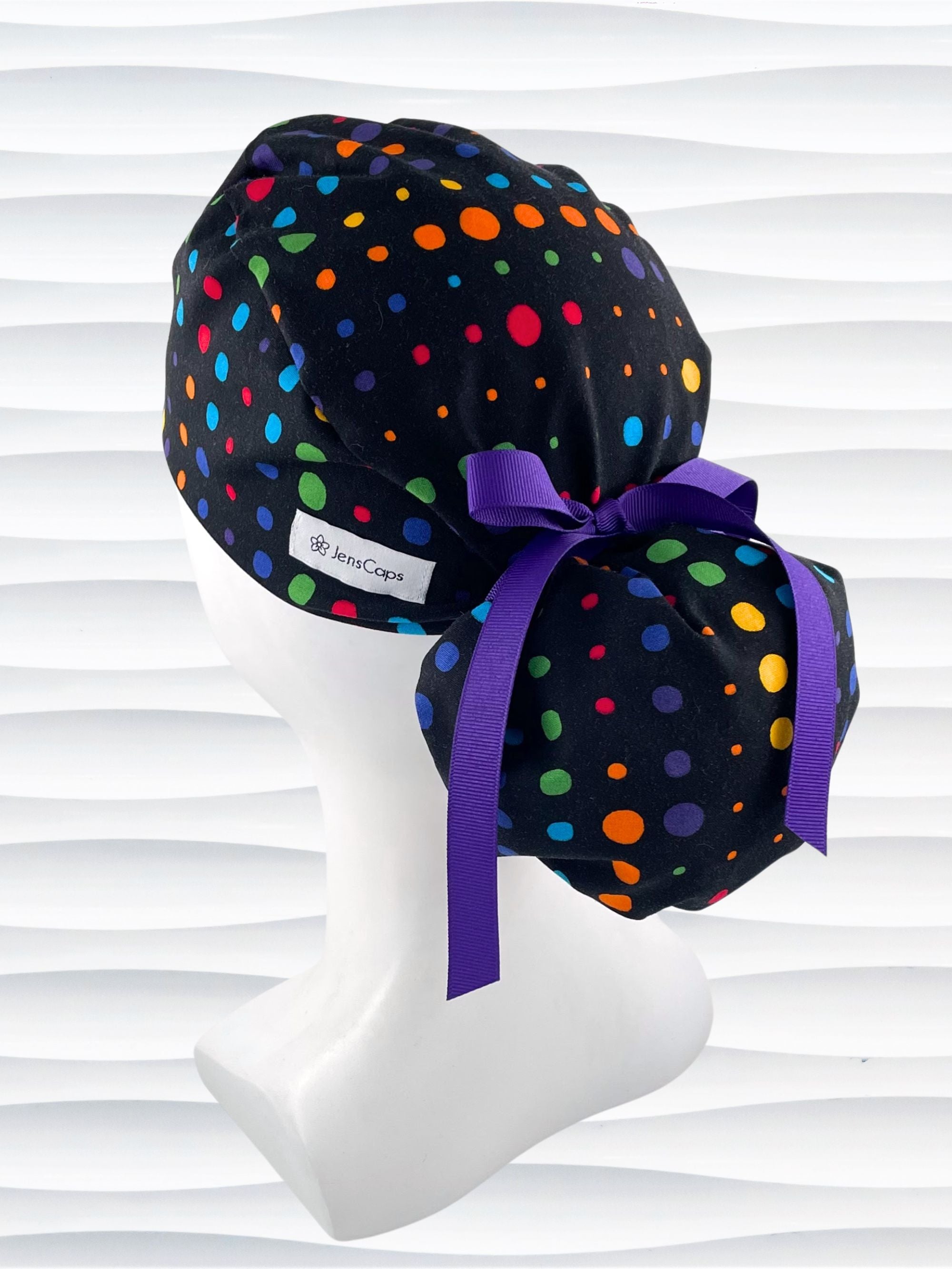 Ponytail style surgical scrub cap hat with circles in primary colors in a linear design on black cotton fabric.