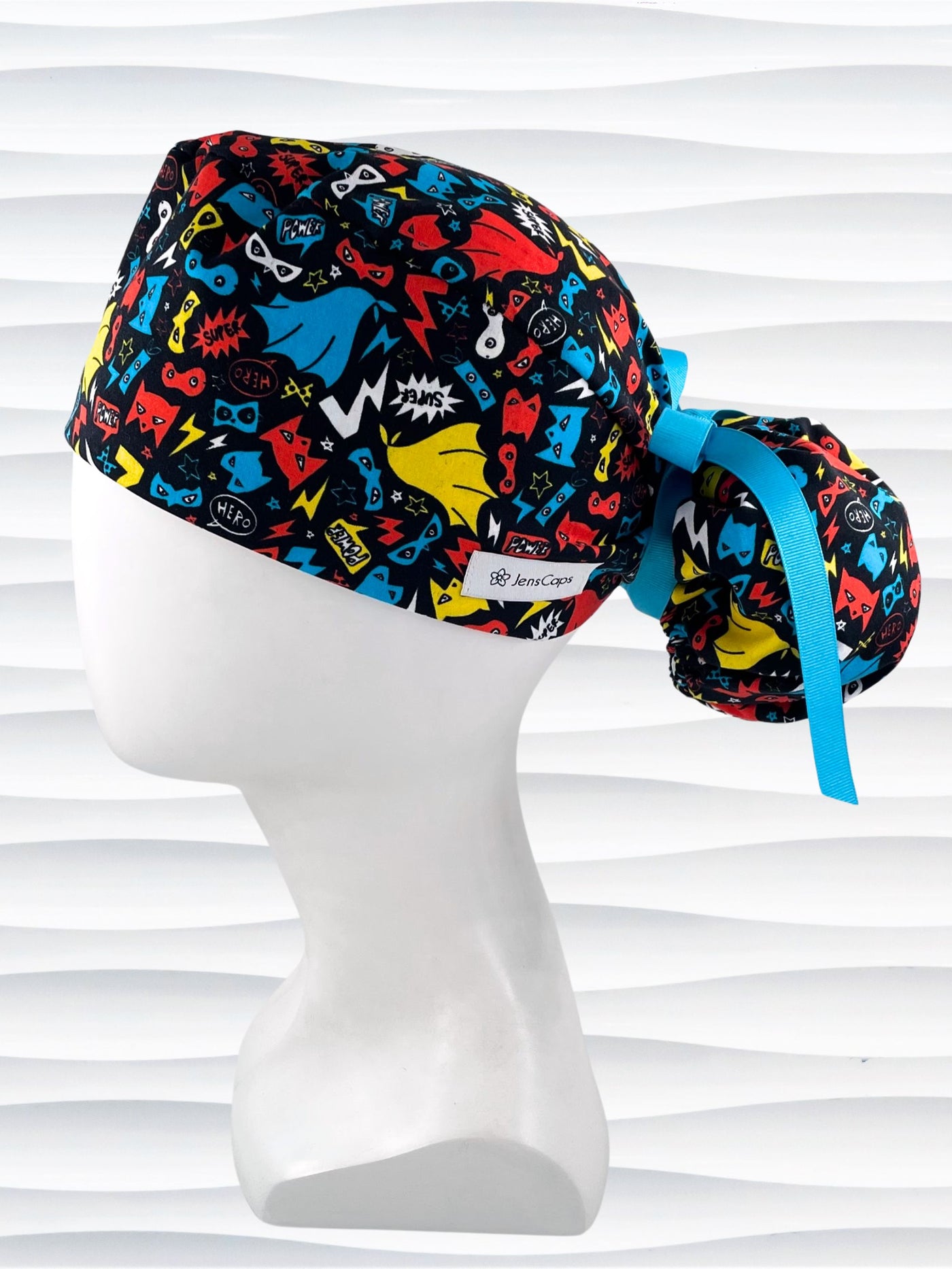 Ponytail style surgical scrub cap hat with superhero masks and capes in red, blue, and yellow on black cotton fabric.