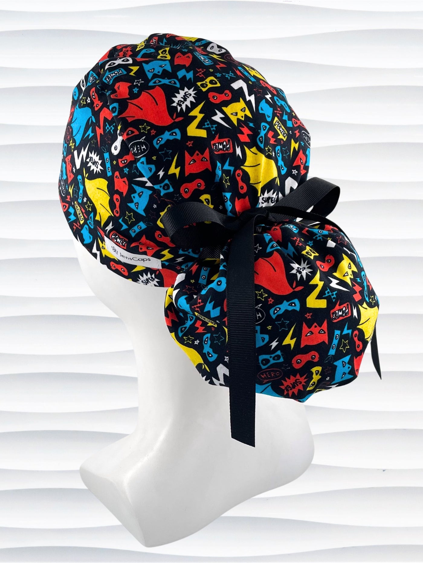 Ponytail style surgical scrub cap hat with superhero masks and capes in red, blue, and yellow on black cotton fabric.