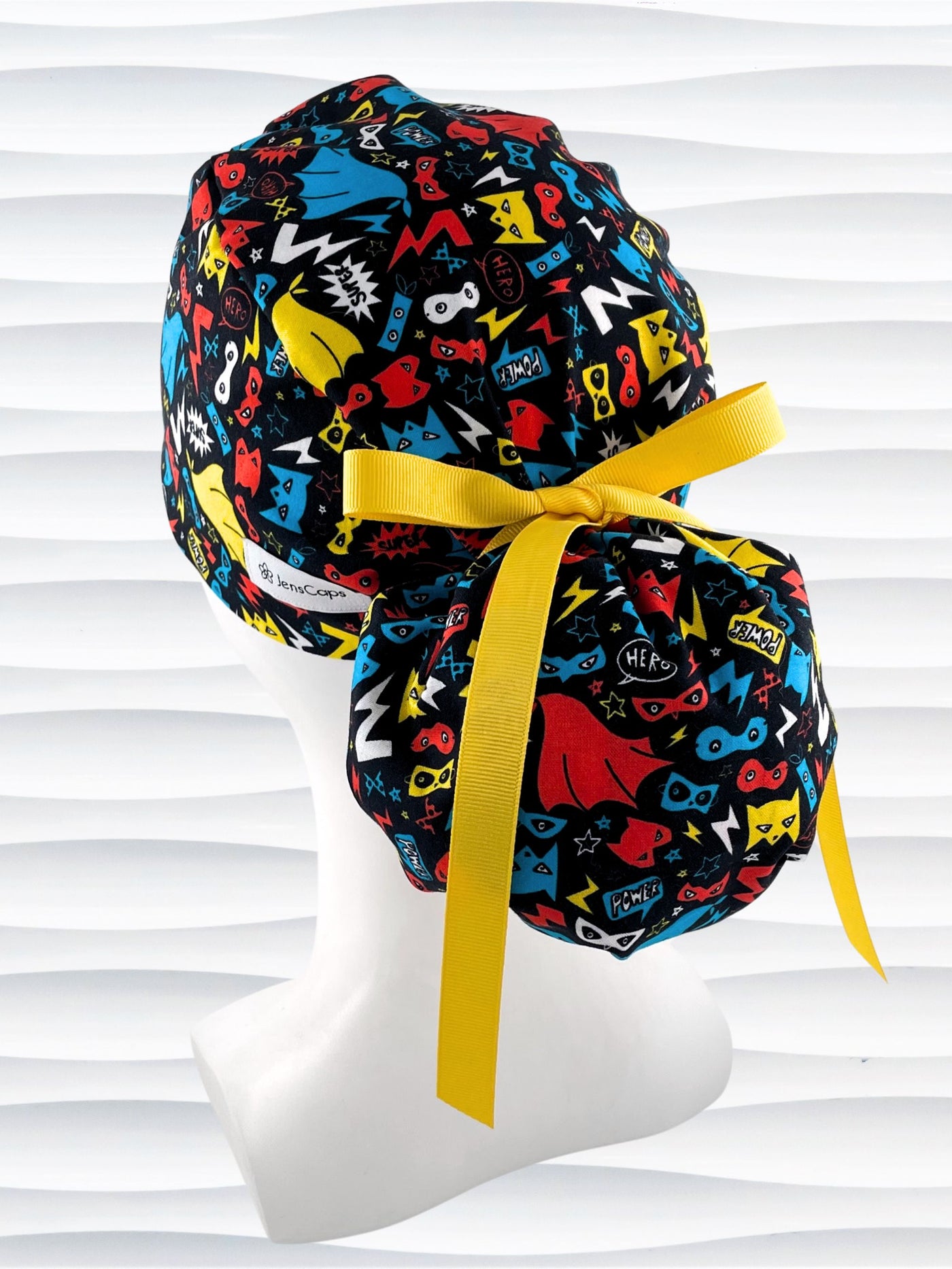 Ponytail style surgical scrub cap hat with superhero masks and capes in red, blue, and yellow on black cotton fabric.