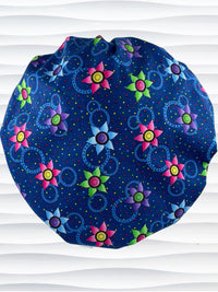Bouffant style surgical scrub cap hat with bright pink, blue, and green flowers and blue circles on dark blue cotton fabric.