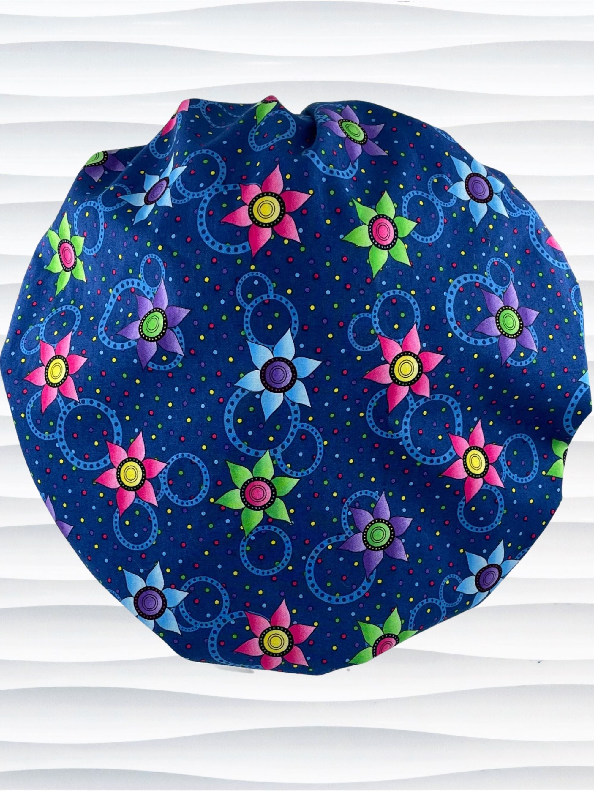 Bouffant style surgical scrub cap hat with bright pink, blue, and green flowers and blue circles on dark blue cotton fabric.