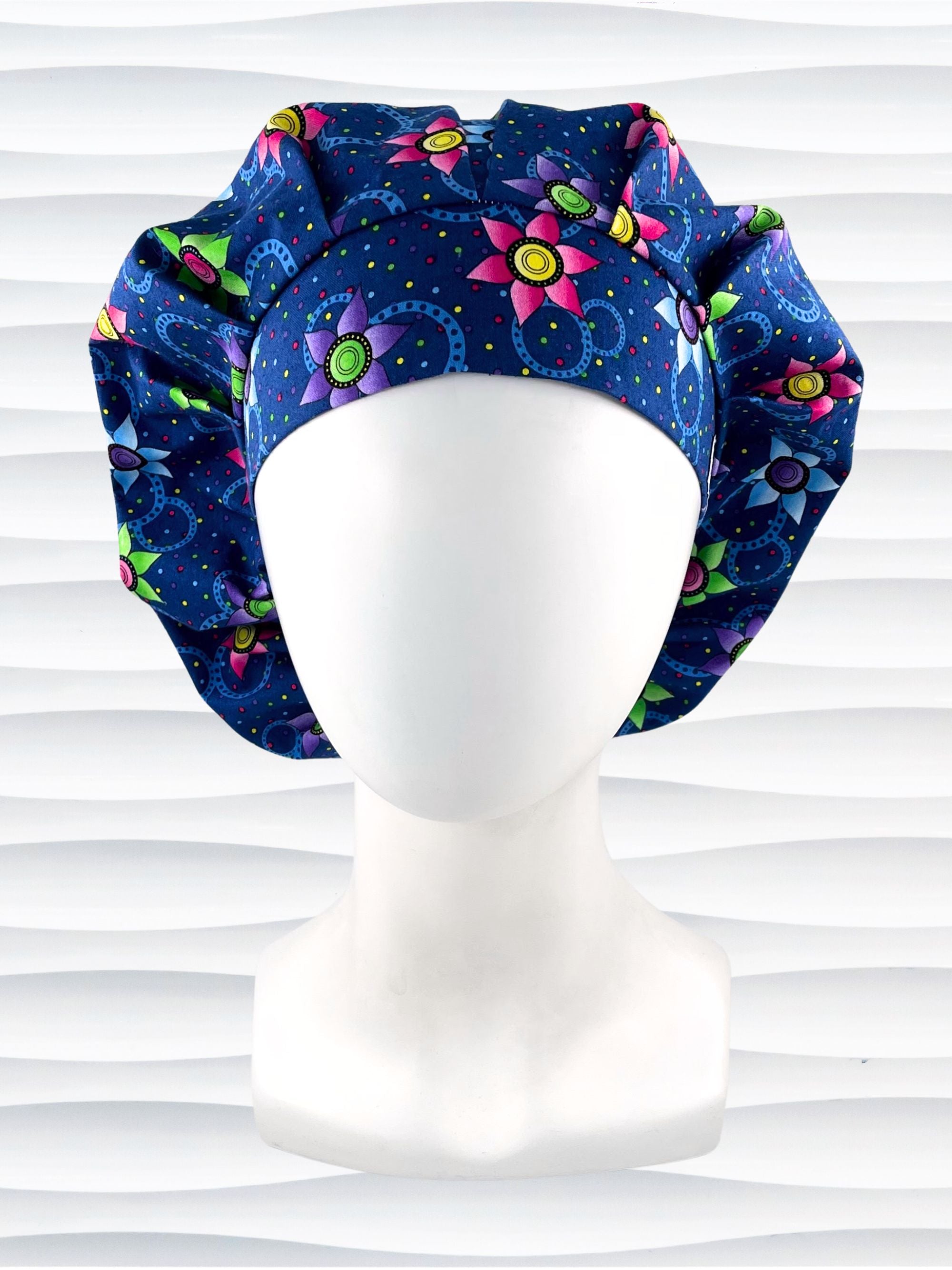 Bouffant style surgical scrub cap hat with bright pink, blue, and green flowers and blue circles on dark blue cotton fabric.