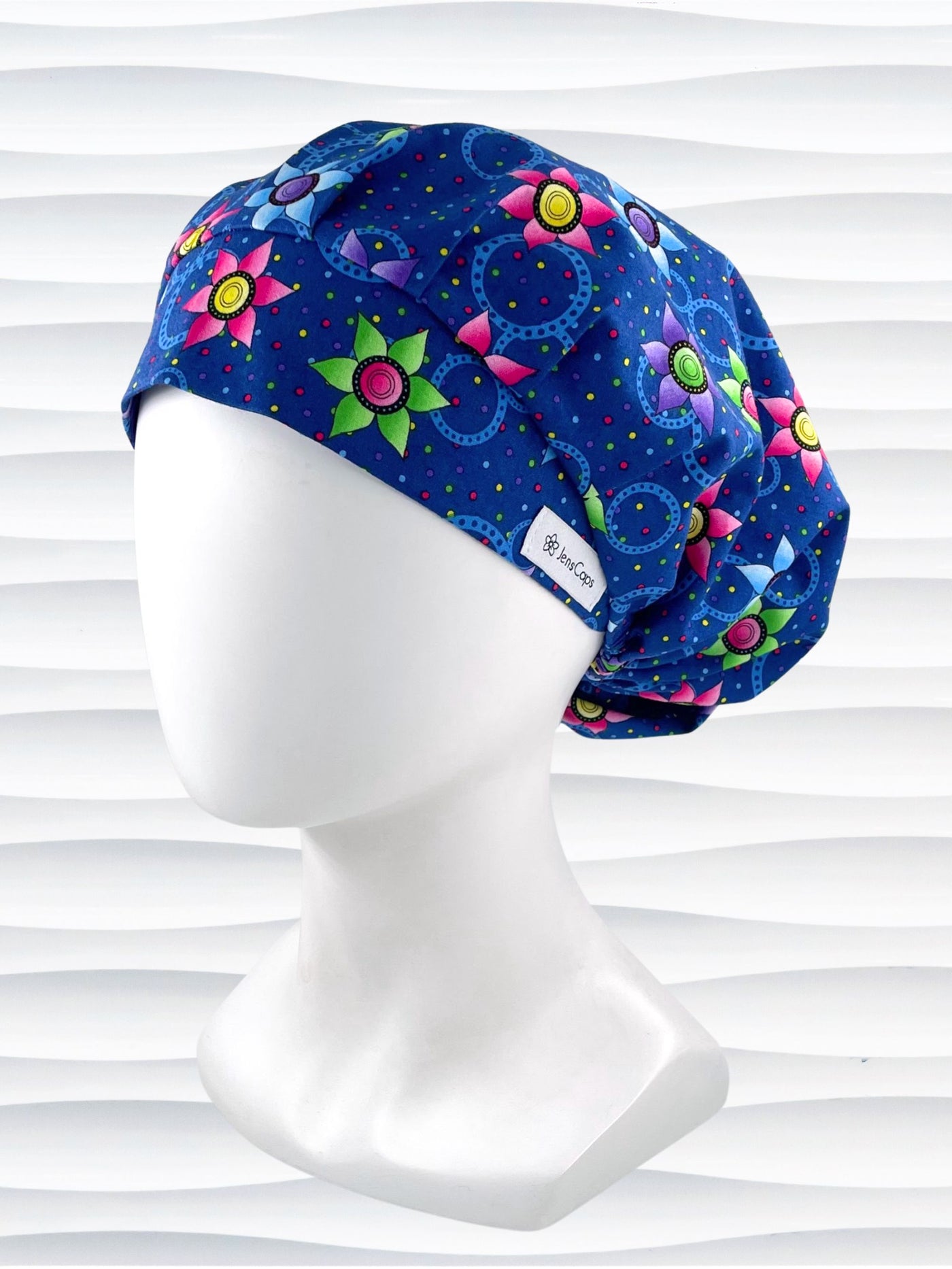 Bouffant style surgical scrub cap hat with bright pink, blue, and green flowers and blue circles on dark blue cotton fabric.