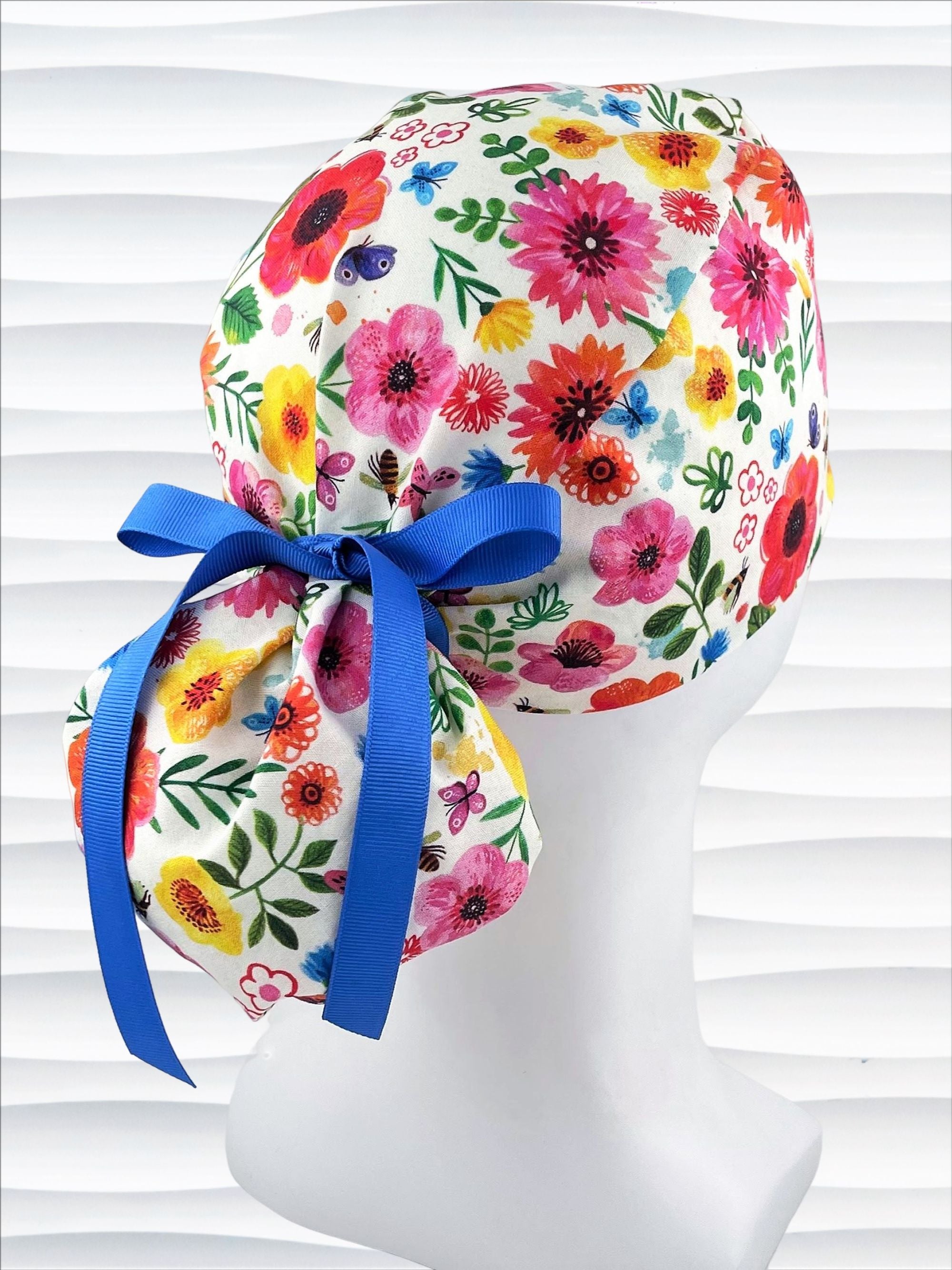 Ponytail style scrub cap hat with flowers and bees and butterflies on white premium cotton and tied with grosgrain ribbon.